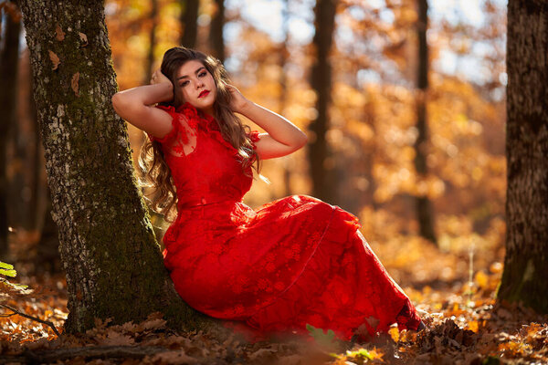 Full length glamorous portrait of a beautiful young woman in red dress in the oak forest