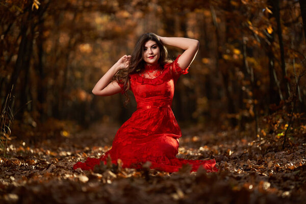 Full length glamorous portrait of a beautiful young woman in red dress in the oak forest