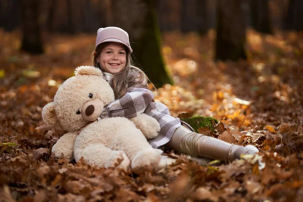 若いです女の子遊びますともに彼女のぬいぐるみで11月下旬にザカラフルなオークの森 — ストック写真