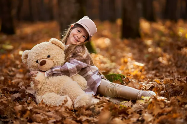 若いです女の子遊びますともに彼女のぬいぐるみで11月下旬にザカラフルなオークの森 — ストック写真
