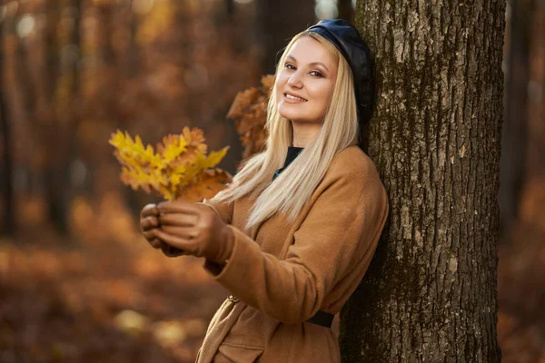 在生机勃勃的橡木森林里 一个身穿大衣戴着帽子的金发年轻女子的自拍直率画像 — 图库照片