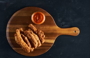 Lezzetli tavuk göğsü şeritleri, kroketler, ahşap tahtaya salsa sosu bandırılmış.