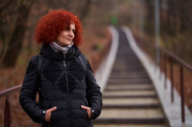 Parkta siyah kışlık ceketli kıvırcık saçlı bir kadının portresi.