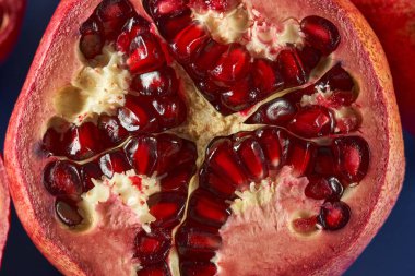 Dilimlenmiş nar meyveleri ve mavi arka planda sulu tohumlar.