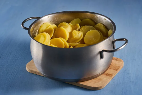 青い木の板の上のステンレス製の鍋で熱々にゆでたジャガイモ — ストック写真