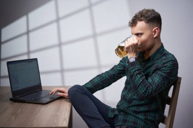 Young business man working at his laptop while drinking a non alcoholic beer from a mug