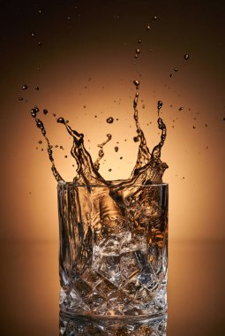 Buzlar viski bardağına altın renginde buz sıçratıyor.