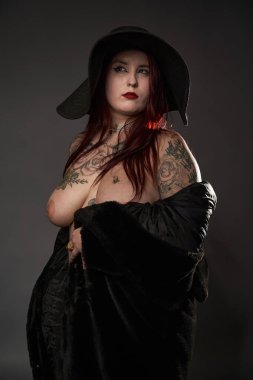 Güzel dövmeli, iri yarı, siyah kürklü ve şapkalı bir kadın.