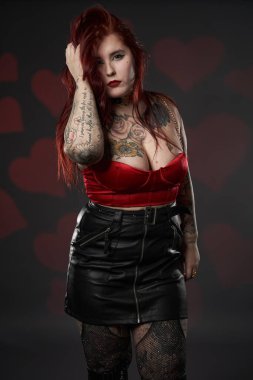 Güzel dövmeli, iri yarı, siyah etekli, kırmızı sütyenli, kapsayıcı ve vücut pozitifliği olan bir kadın.