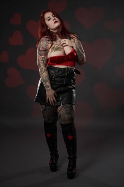 Güzel dövmeli, iri yarı, siyah etekli, kırmızı sütyenli, kapsayıcı ve vücut pozitifliği olan bir kadın.