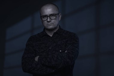 Arka planda pencere gölgesi olan orta yaşlı bir iş adamının soğuk tonlu portresi.