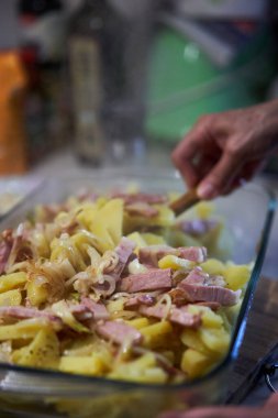 Patatesle karıştırılmış jambon hazırlıyorum. Parmesanla süslenmiş ve cam tepside otlar var.