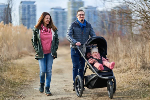 若いです家族とともに彼らの小さな赤ちゃんの女の子歩く公園で赤ちゃん馬車で住宅地 — ストック写真