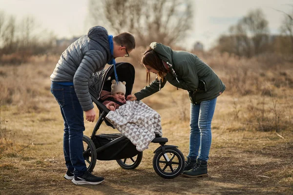 若いです家族とともに彼らの小さな赤ちゃんの女の子歩く公園で赤ちゃん馬車で住宅地 — ストック写真