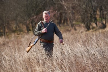 Tüfekli bir avcı ormandaki çayırlarda yürüyor.