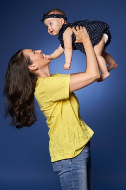 Genç anne, küçük kızıyla harika vakit geçiriyor. Stüdyo, mavi arka planda çekim yapıyor.