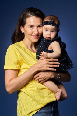 Genç anne, küçük kızıyla harika vakit geçiriyor. Stüdyo, mavi arka planda çekim yapıyor.