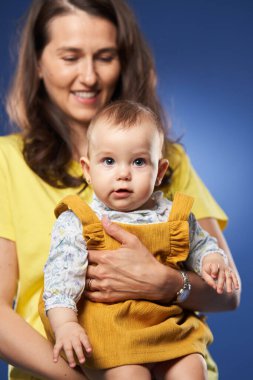 Genç anne, küçük kızıyla harika vakit geçiriyor. Stüdyo, mavi arka planda çekim yapıyor.