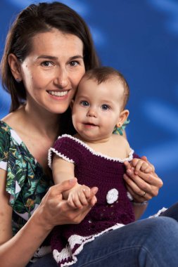 Genç anne, küçük kızıyla harika vakit geçiriyor. Stüdyo, mavi arka planda çekim yapıyor.