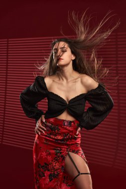 Kırmızı etekli, siyah bluzlu, saçları rüzgarda uçuşan güzel bir model.