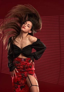 Kırmızı etekli, siyah bluzlu, saçları rüzgarda uçuşan güzel bir model.