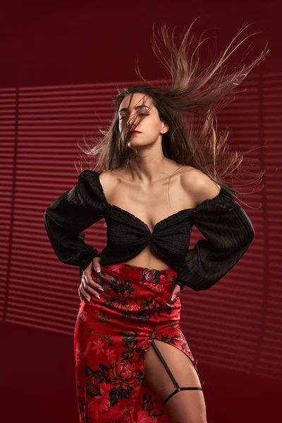 Kırmızı etekli, siyah bluzlu, saçları rüzgarda uçuşan güzel bir model.