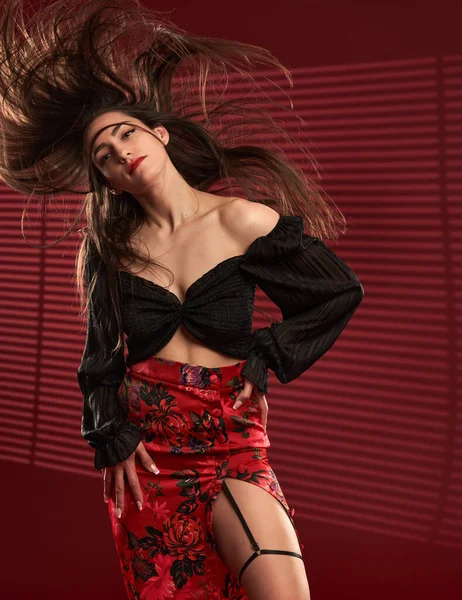 Kırmızı etekli, siyah bluzlu, saçları rüzgarda uçuşan güzel bir model.