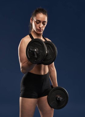 Güçlü, güzel bir kadın halterlerle bisepsi kıvırıyor, ayakta duruyor.