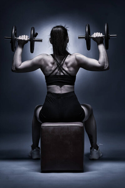 Woman doing shoulder workout with dumbbells, seen from the back