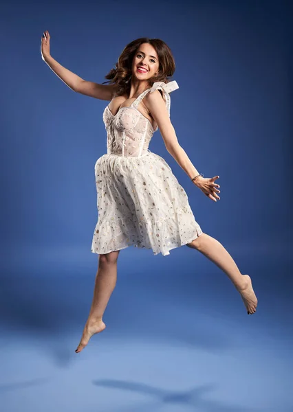 Portrait Beautiful Young Woman White Dress Jumping Joy Blue Background — Zdjęcie stockowe