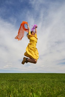 Sarı elbiseli mutlu genç kadın güneşli bir günde yeşil buğday tarlasına atlıyor.