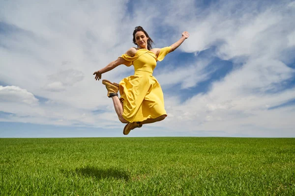 在阳光灿烂的日子里 穿着黄色衣服的快乐的年轻女子跳到户外的青麦地上 — 图库照片
