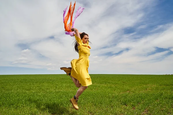 在阳光灿烂的日子里 穿着黄色衣服的快乐的年轻女子跳到户外的青麦地上 — 图库照片