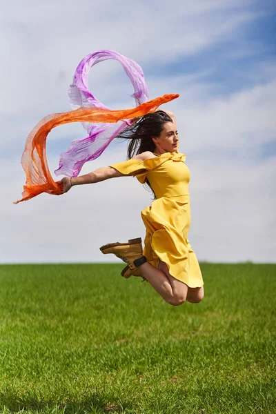 在阳光灿烂的日子里 穿着黄色衣服的快乐的年轻女子跳到户外的青麦地上 免版税图库图片
