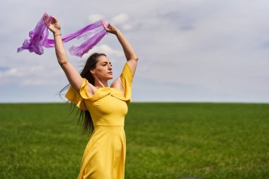 Güneşli bir günde yeşil buğday tarlasında sarı elbiseli genç bir kadın.