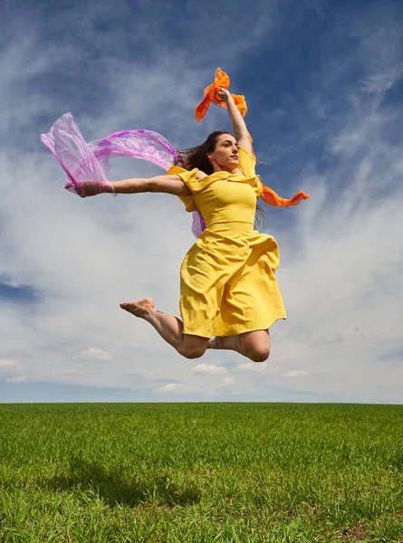 在阳光明媚的日子里 一位身穿黄色衣服的年轻貌美女子在青麦田里高兴地跳起舞来 拍下了一个动作镜头 — 图库照片