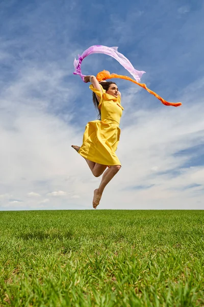 在阳光明媚的日子里 一位身穿黄色衣服的年轻貌美女子在青麦田里高兴地跳起舞来 拍下了一个动作镜头 — 图库照片