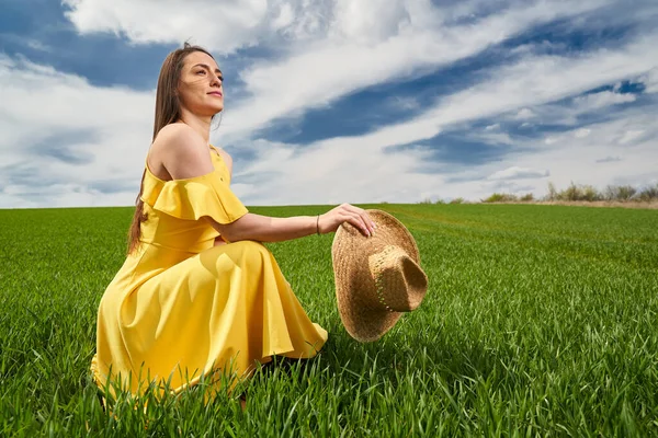 晴れた日に緑の小麦畑に黄色のドレスと麦藁帽子の若い女性 — ストック写真