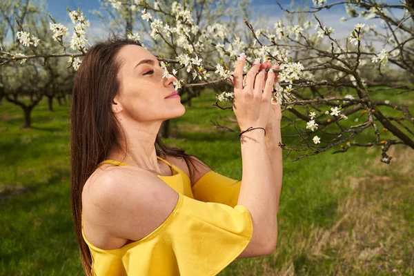 Çiçek açan erik bahçesinde sarı elbiseli mutlu ve çekici bir kadın.