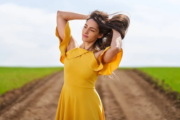 麦畑の間の未舗装の道路上の黄色のドレスの若い女性 — ストック写真