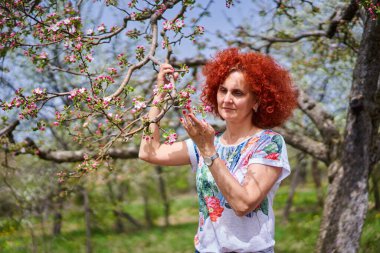 Kıvırcık kızıl saçlı çiftçi kadın elma bahçesinde çiçek açmış.
