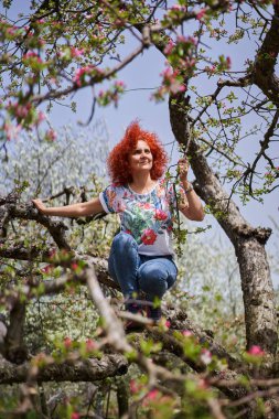 Kıvırcık kızıl saçlı çiftçi kadın elma bahçesinde çiçek açmış.