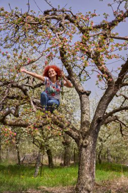 Kıvırcık kızıl saçlı çiftçi kadın elma bahçesinde çiçek açmış.