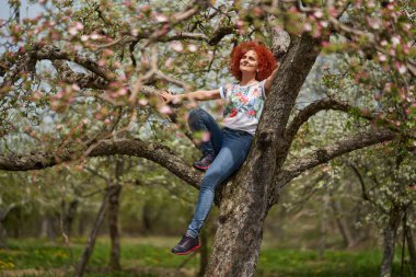 Kıvırcık kızıl saçlı çiftçi kadın elma bahçesinde çiçek açmış.