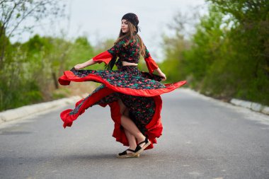Caddenin ortasında dans eden genç, güzel çingene kadın, geleneksel kostümlü.