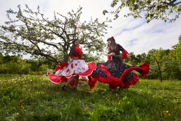 開花リンゴの果樹園で踊る伝統的なジプシーの衣装の2人の若い女性 — ストック写真