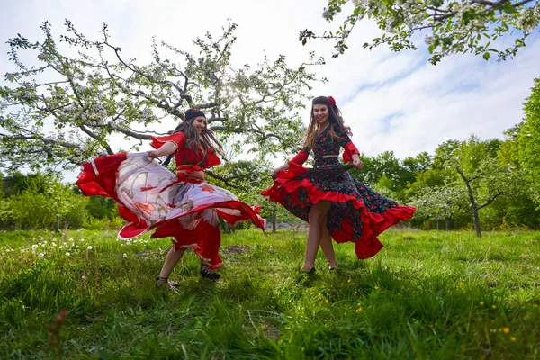 開花リンゴの果樹園で踊る伝統的なジプシーの衣装の2人の若い女性 — ストック写真