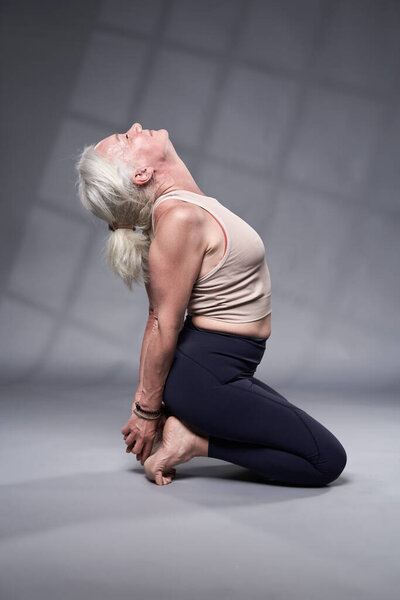 Старшая женщина с седыми волосами йога, студия снята на сером фоне