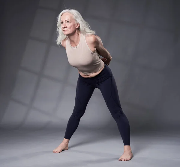 老年妇女与白发训练瑜伽 工作室拍摄灰色背景 — 图库照片