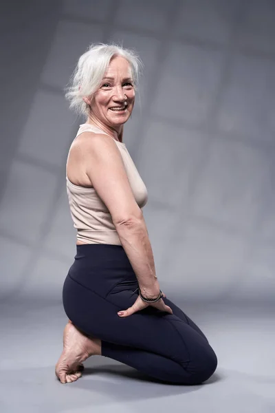 老年妇女与白发训练瑜伽 工作室拍摄灰色背景 图库照片